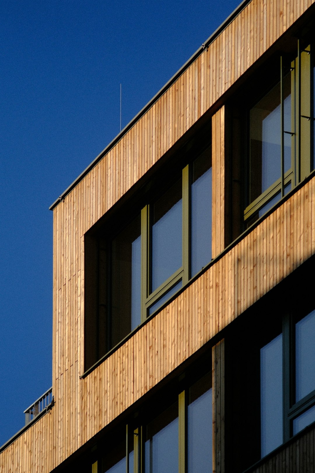 Modern building facade with vertical wooden cladding and dark windows.